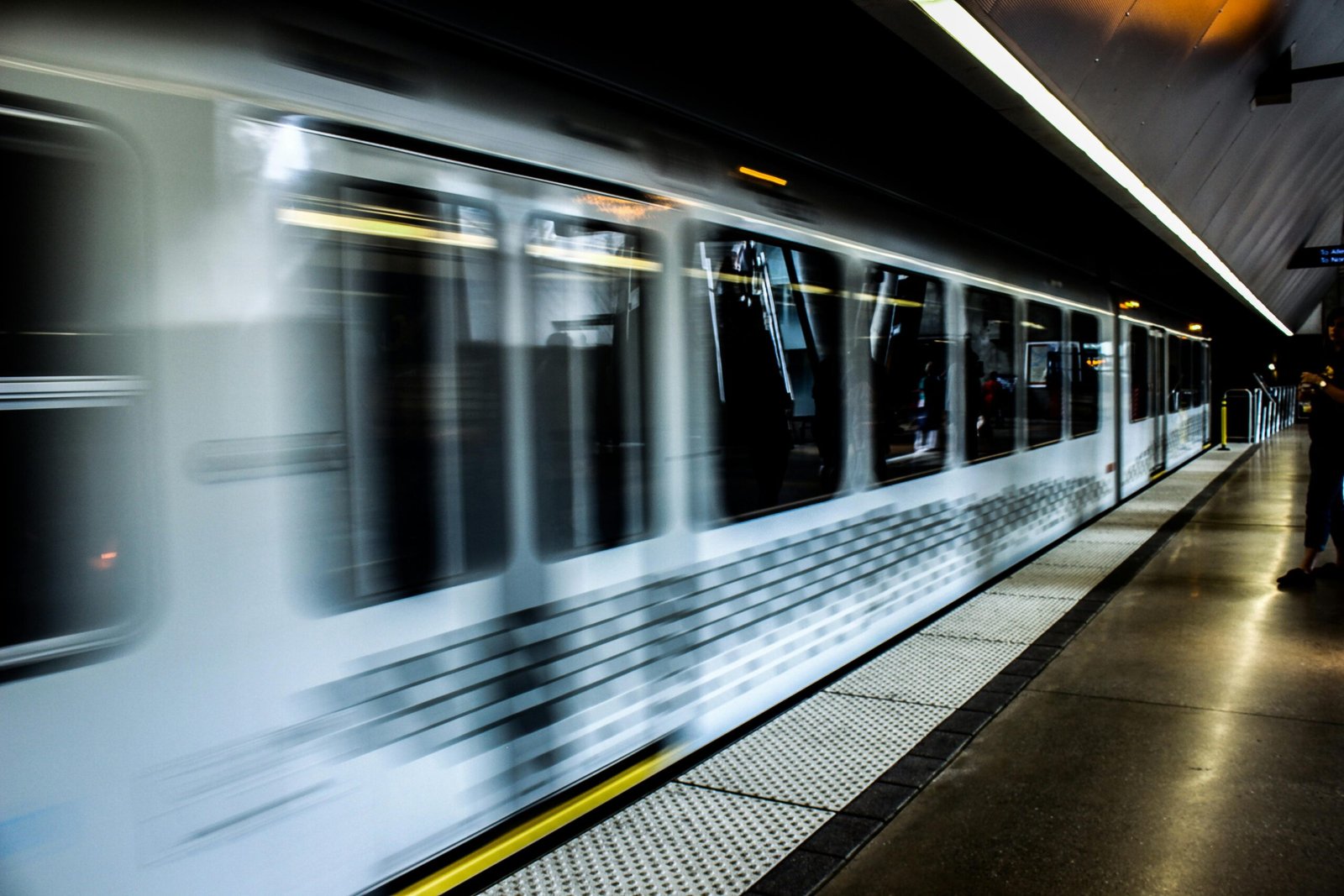 Blurred image of a modern train speeding through a dimly lit station platform.